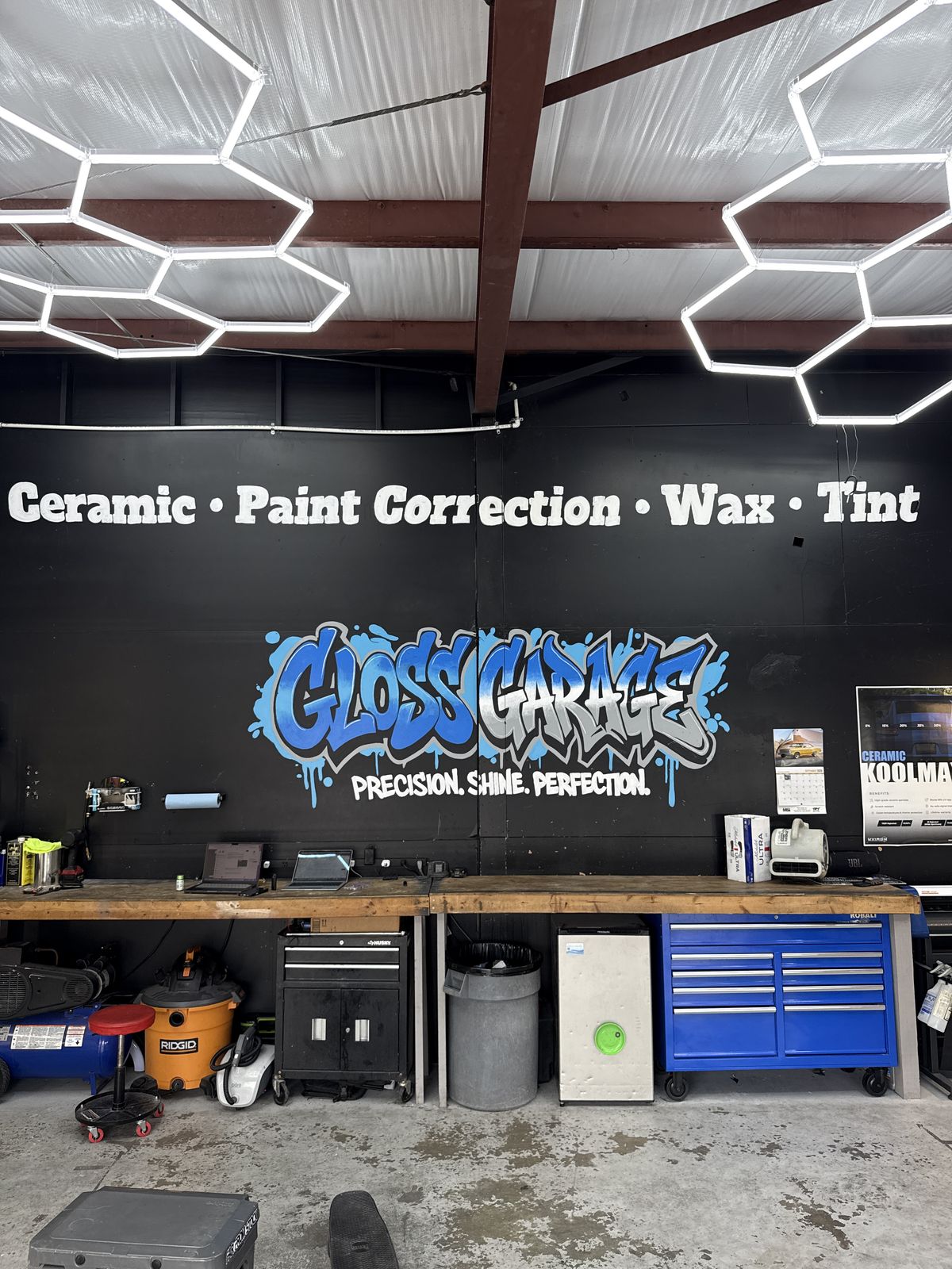 Inside the Gloss Garage shop in Venice: blue graffiti Gloss Garage mural under hexagon LED ceiling lights, with Ceramic, Paint Correction, Wax and Tint painted on the wall