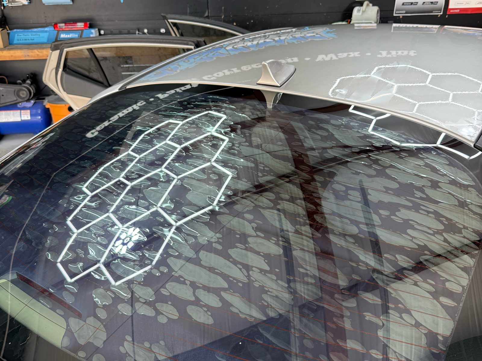 Freshly tinted rear window on a silver sedan reflecting the hexagon shop lights