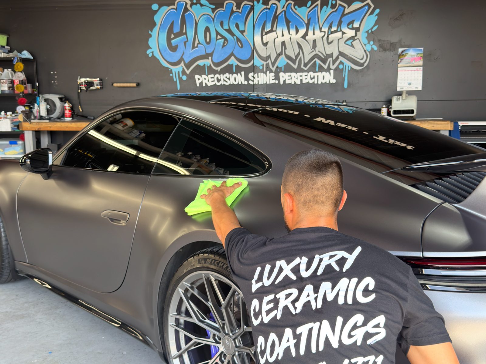 Cody Noland wiping down a wrapped Porsche 911 under the Gloss Garage mural
